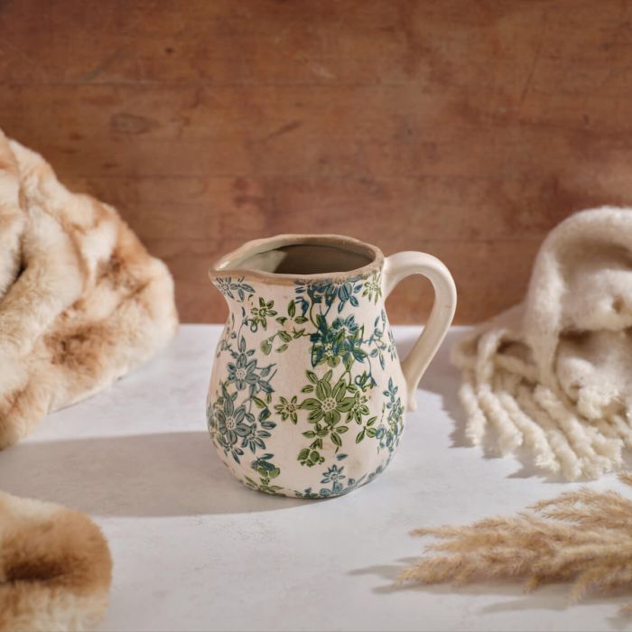 Cream ceramic decorative jug featuring green and blue vintage floral motifs, curved handle, spout, and subtle crackle glaze